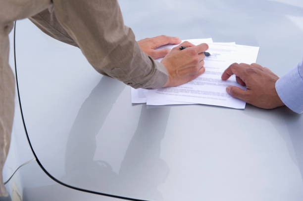 Deux personnes qui parcourent un document officiel sur le capot d'une voiture